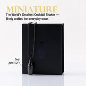 Miniature black cocktail shaker necklace in front of a black gift box.