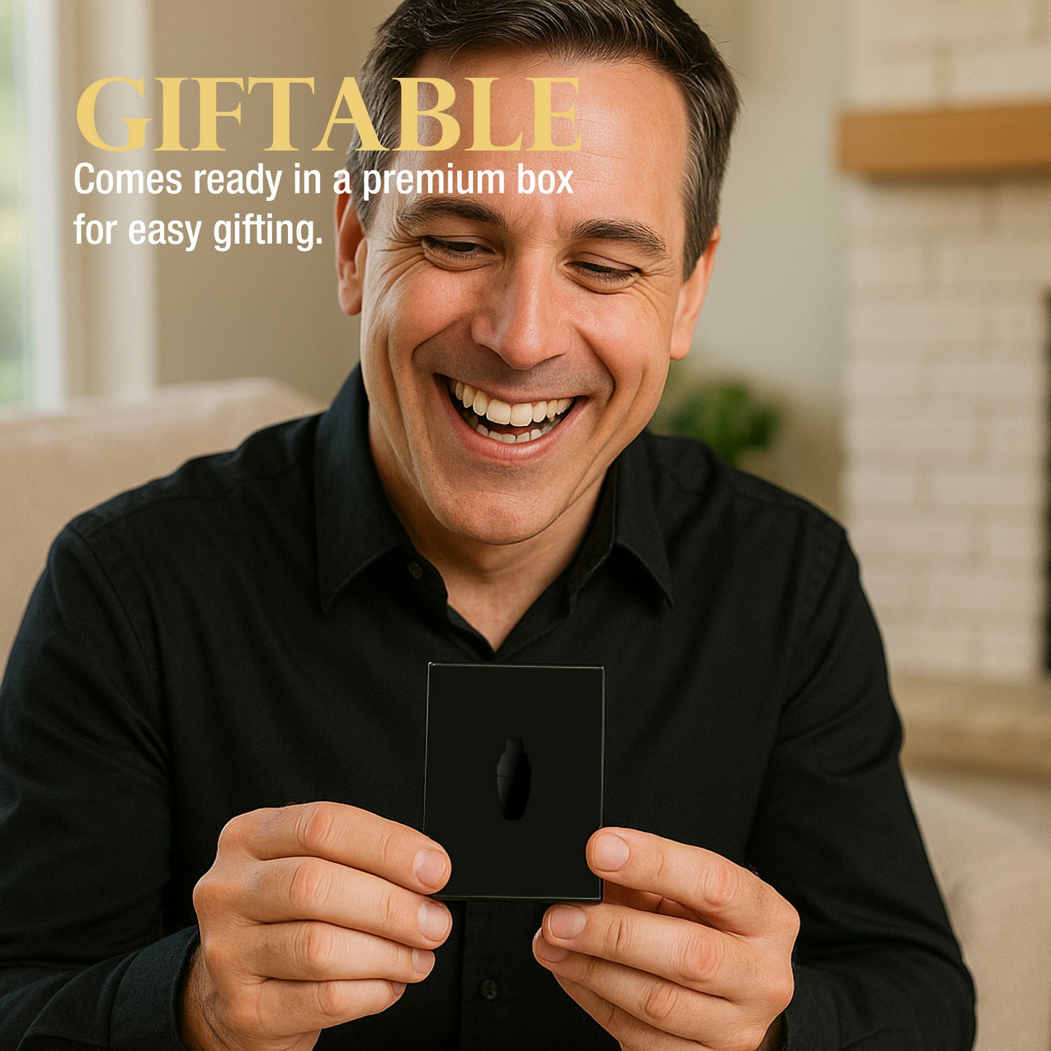 Man holding a small black gift box with a black logo, smiling, in a home setting.