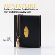 Miniature gold cocktail shaker necklace in front of a black gift box.